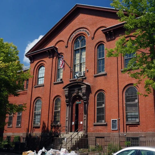Red brick building with large windows and a flag on a clear day