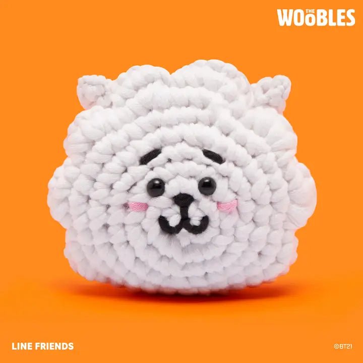 White plush toy with black accents on an orange background, featuring the Woobles brand.