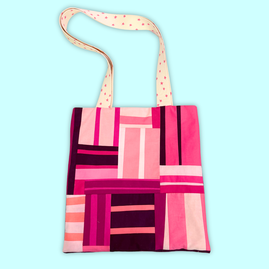 Pink patchwork tote with white handles on a blue background.