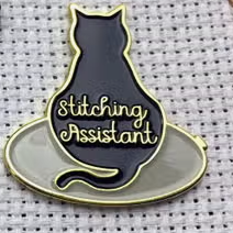 Needle minder with a cat sitting on an embroidery hoop with the text "Stitching Assistant"