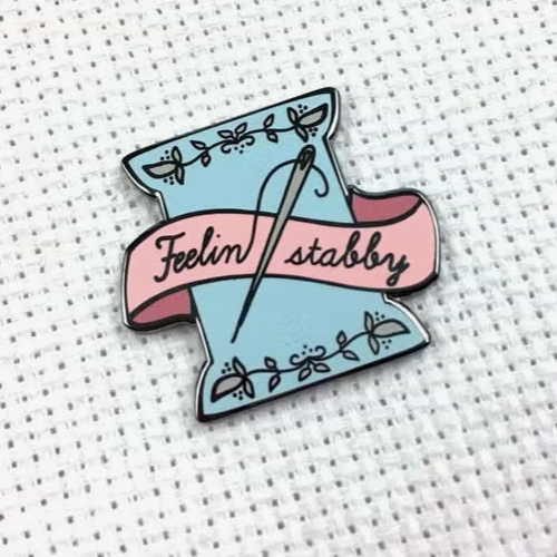 Needle minder featuring a floss spool along with a needle and thread spelling out the phrase "Feeling stabby"