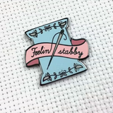 Needle minder featuring a floss spool along with a needle and thread spelling out the phrase 