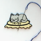 Needle minder with grey kitty asleep on top of an embroidery hoop 