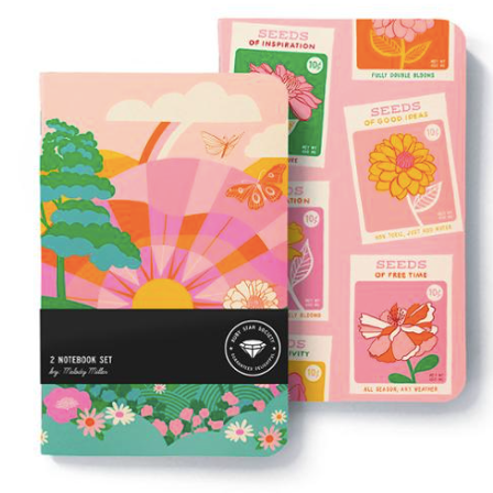 display image of notebook set  both pink one shows sun rising over a flowery field and the other shows seed packets with flowers and phrases like "seeds of good ideas" on them