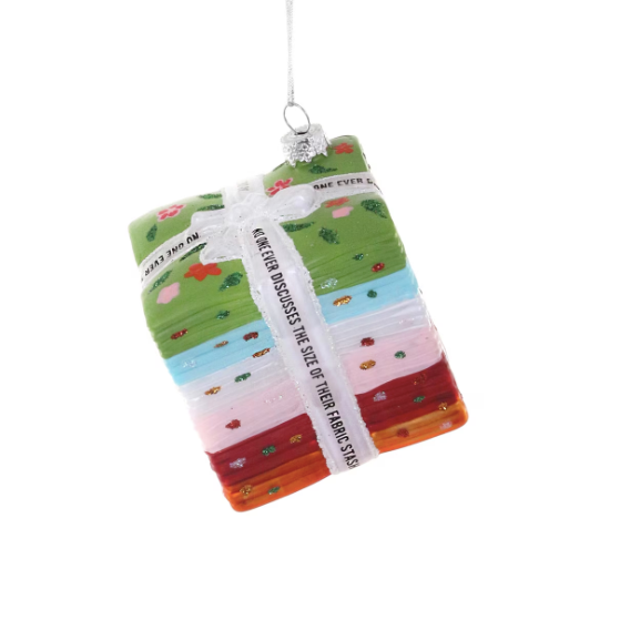 glass ornament of a stack colorful patterned fabric with a white bow on a white background