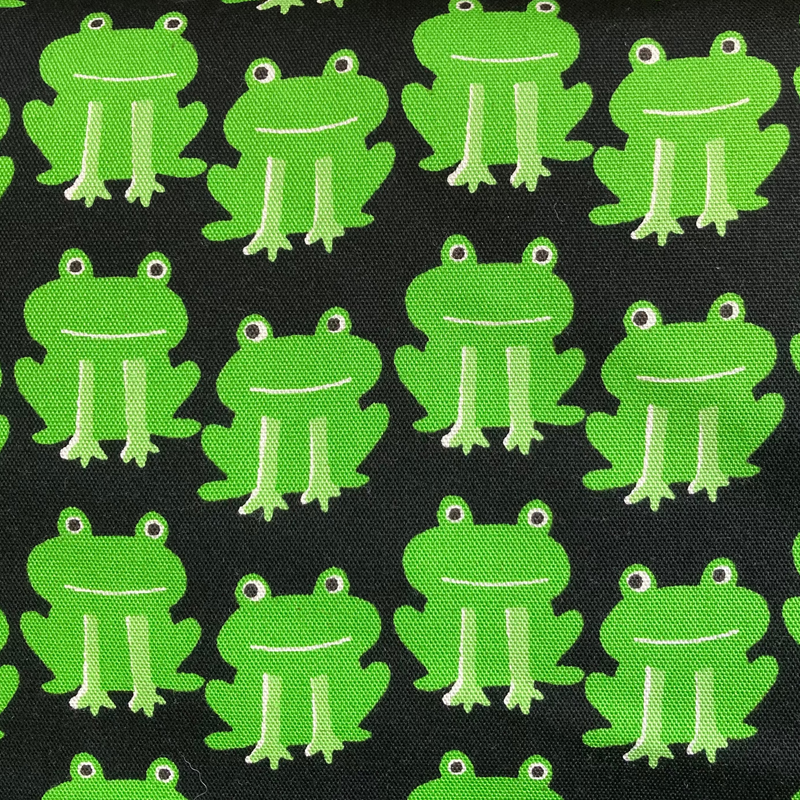 Happy green frogs line up on a black background in this canvas fabric from Sevenberry