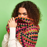 Person wearing finished crocheted cowl from kit. Orange pink and green colors. 