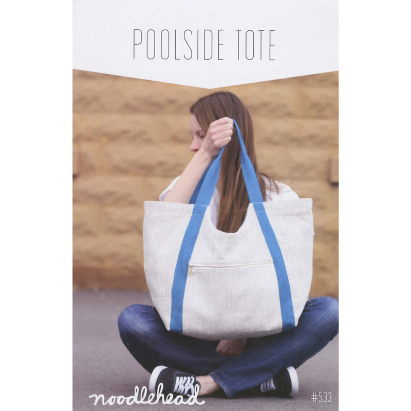 Woman holding a white tote bag with blue straps against a wooden background, featuring 'noodlehead' branding.