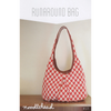 Red and white patterned bag with brown handle on a wooden surface, against a plain background.