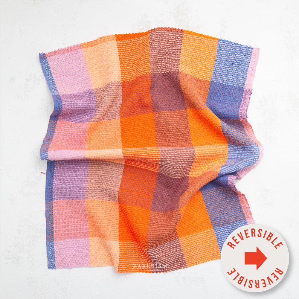 Textured fabric swatch with pink, orange, and blue checkered pattern. Sticker in front says "reversible" 
