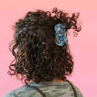 Person with curly hair wearing a colorful yarn skein hair clip on a pink background