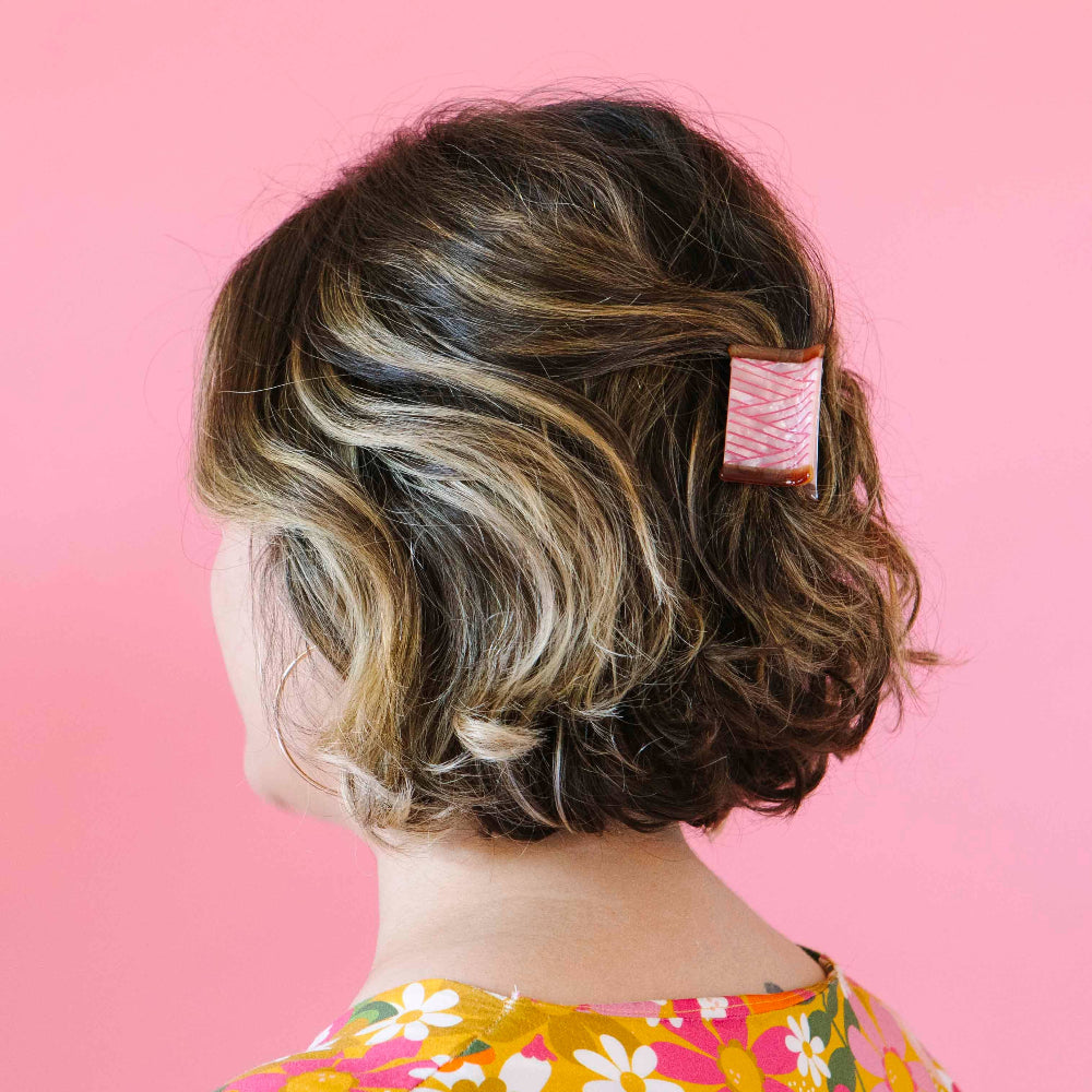 Person with styled hair featuring a pink hair clip against a pink background