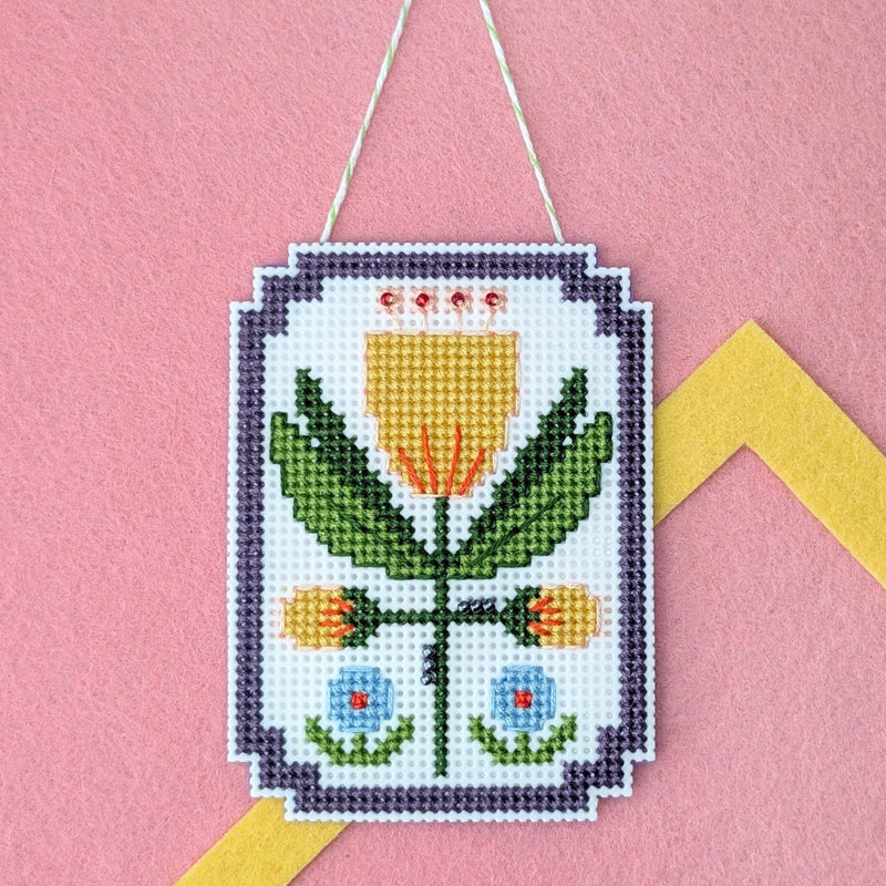 Framed tulip cross stitch on a pink felt background with a yellow felt frame
