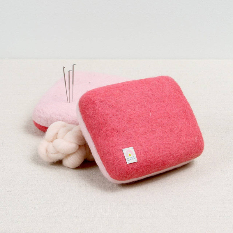 Pink wool needle felting mat with white fiber and needle felting needles on a white background
