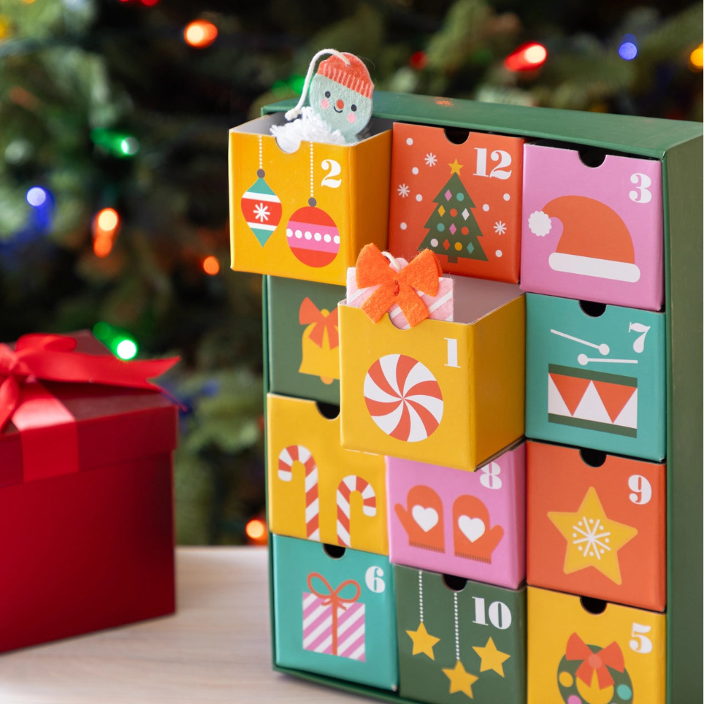 A colorful advent calendar with numbered drawers is pictured in front of a Christmas tree.