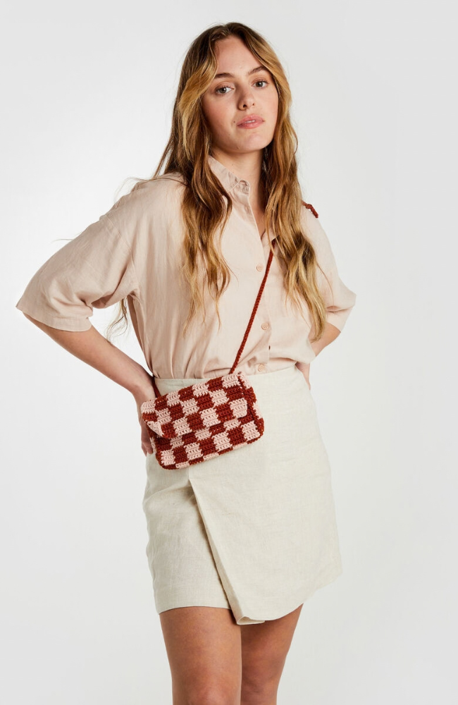 Model in beige shirt and white skirt with a cream and burgundy checkered crossbody bag on a white background.