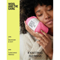 Person holding a pink yarn ball with 'Wool and the Gang' label on a yellow background