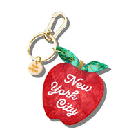 Charm in the shape of a red apple with white text reading "New York City" attached to a gold keychain ring.
