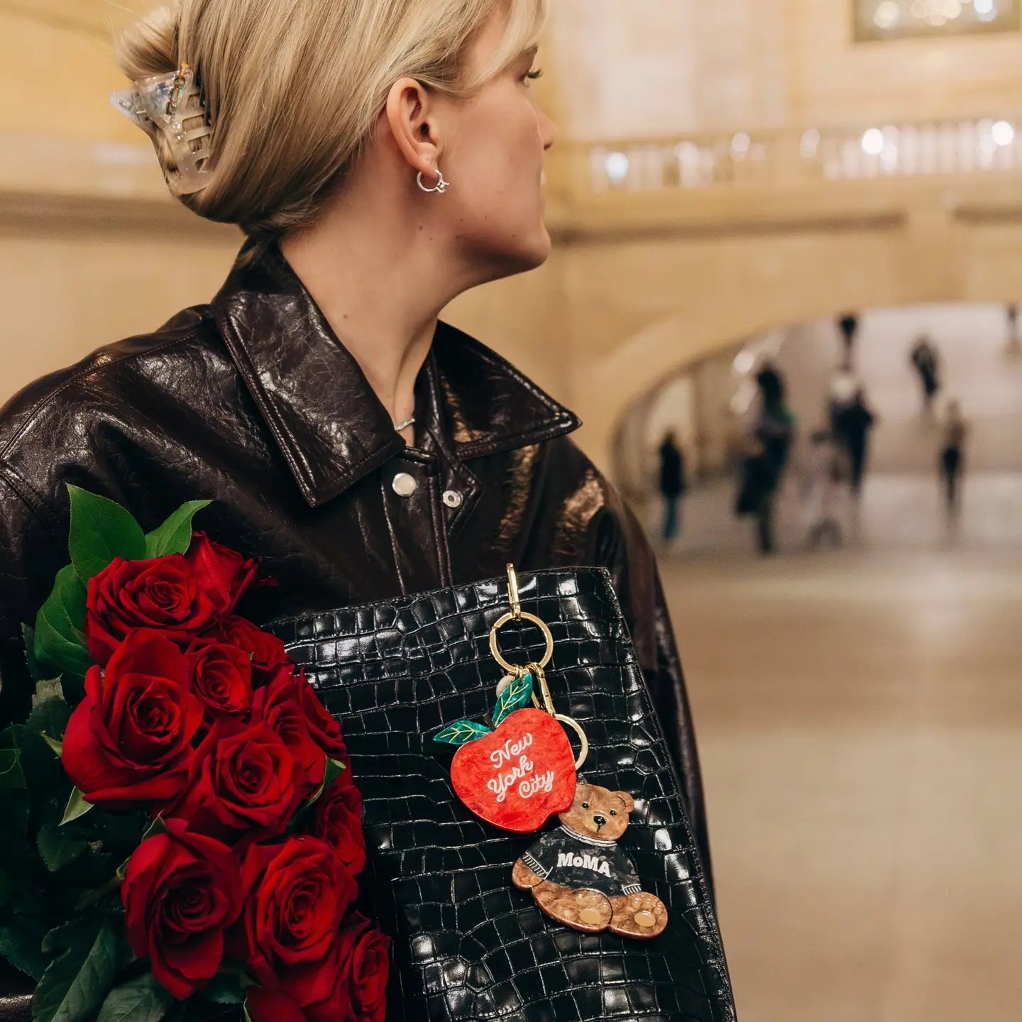 Person holding red roses and a black textured bag with multiple keychains in a blurred indoor setting