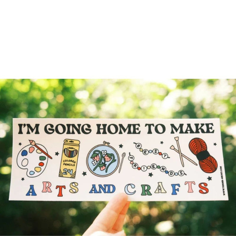 Sticker with 'I'm going home to make arts and crafts' text and illustrations held against a blurred green background.