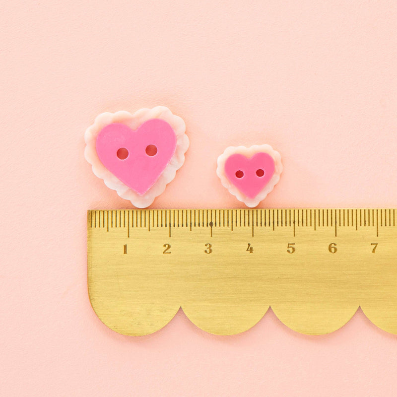 Two heart-shaped buttons with a gold ruler on a pink background