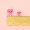 Two heart-shaped buttons with a gold ruler on a pink background
