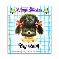 Vinyl sticker with a cute illustration of a black kitten with bows and 'Cry Baby' text on a blue grid background.