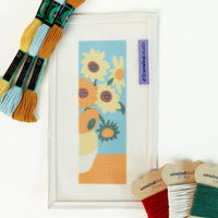 Needlepoint kit with sunflower design and embroidery threads on a white background