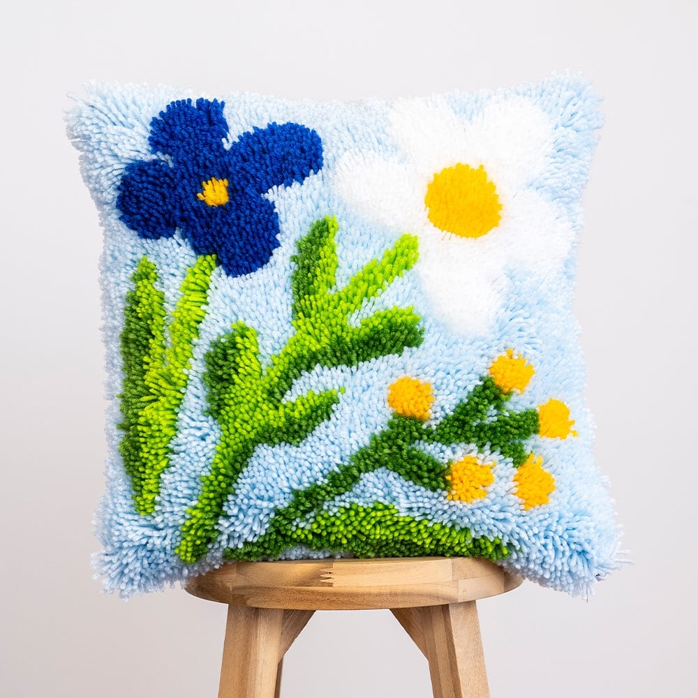 A fluffy pillow cushion featuring blue and white flowers with green stems on a pale blue background.
