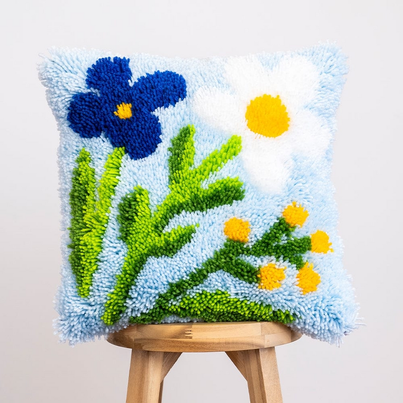A fluffy pillow cushion featuring blue and white flowers with green stems on a pale blue background.