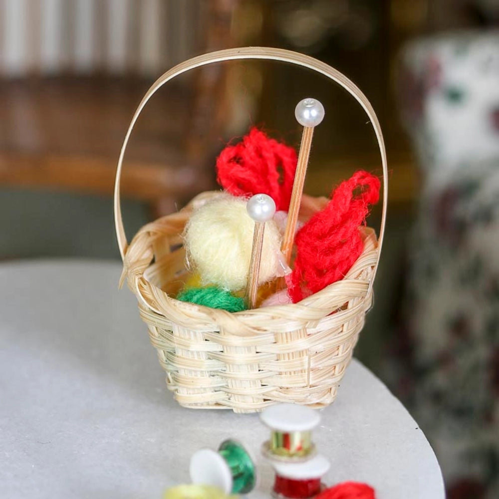 Miniature wicker basket with yarn and knitting needles on a table.