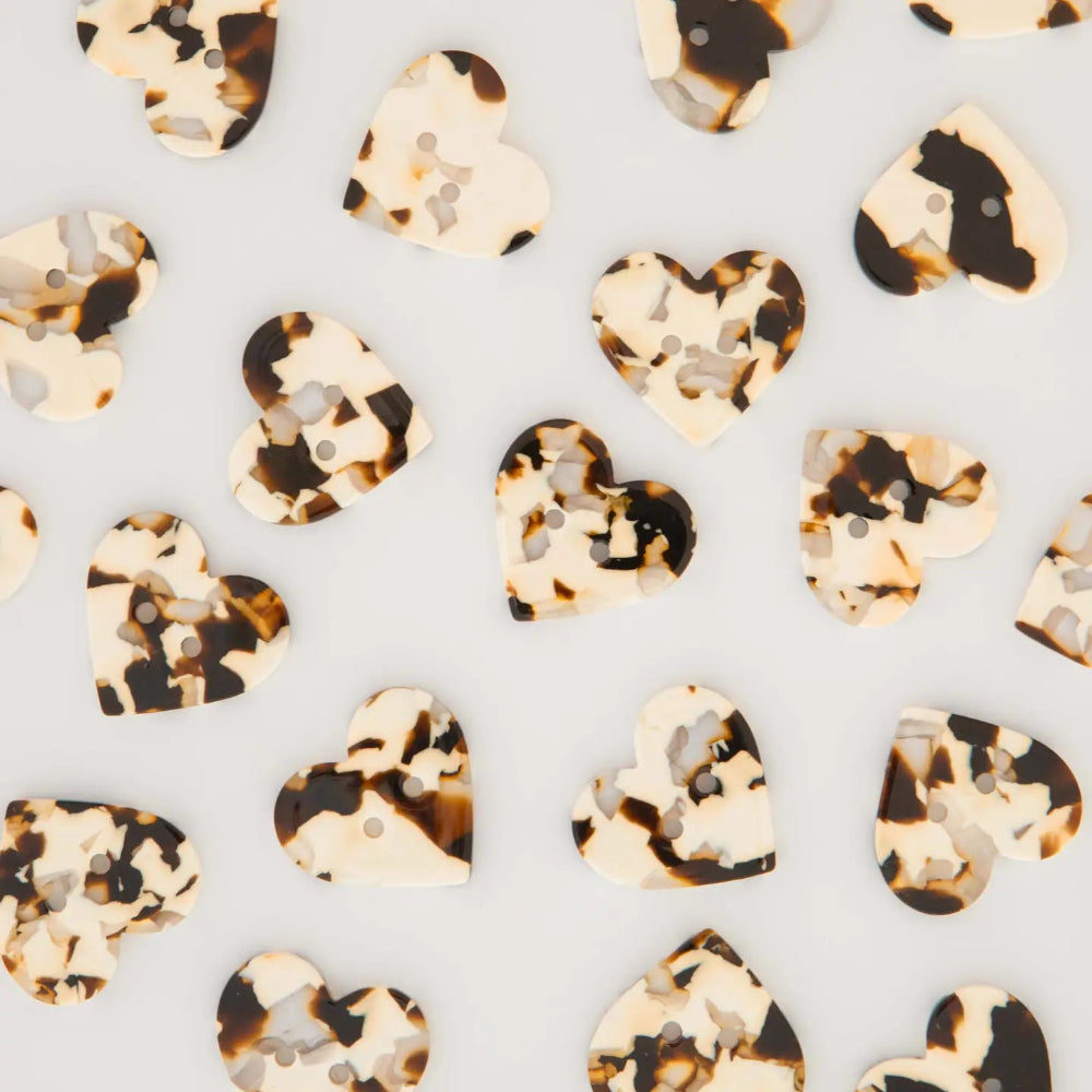 Heart-shaped tortoiseshell buttons with two buttonholes, scattered on a light gray background.