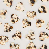 Heart-shaped tortoiseshell buttons with two buttonholes, scattered on a light gray background.