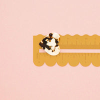 A small tortoiseshell button is shown on a yellow plastic ruler against a solid pink background.