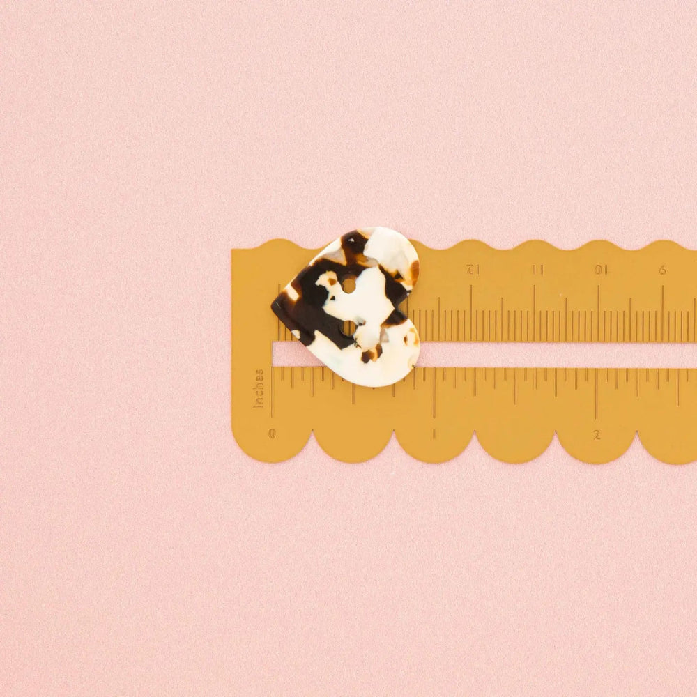 A small tortoiseshell button is shown on a yellow plastic ruler against a solid pink background.