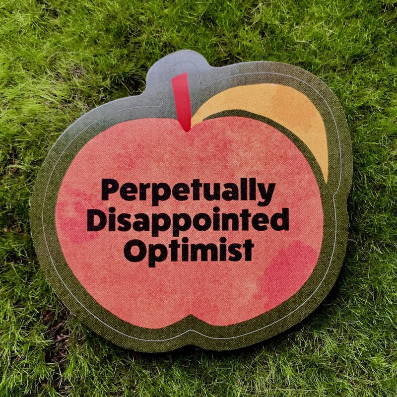 Peach shaped sticker with black text reading "perpetually disappointed optimist"
