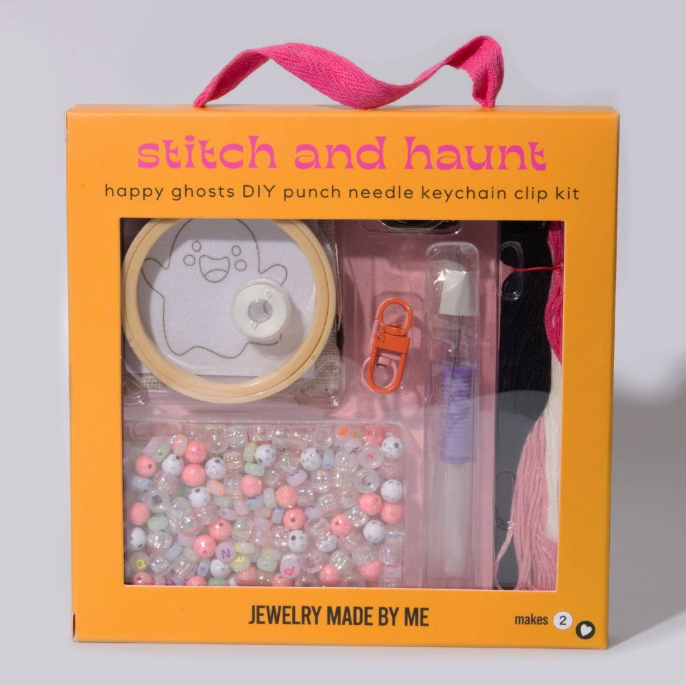 A DIY punch needle keychain kit in an orange gift box with a pink handle. The kit includes a spool of light tan thread, a ghost design template, a pink punch needle clip, a clear pen, and a tray of assorted pastel beads.