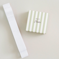 A white knit elastic laid diagonally next to its light green and white striped gift box labeled 'KNIT Classic' on a warm off-white background.