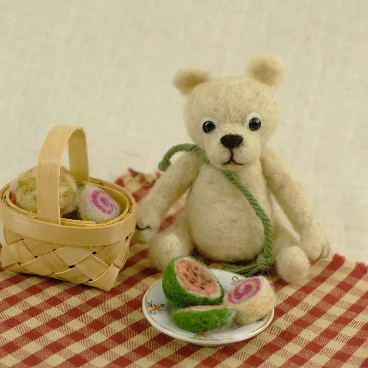 Teddy bear with a basket and fruit on a checkered tablecloth