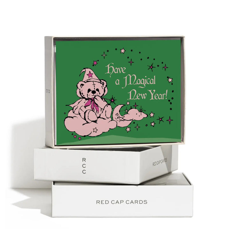 Green card with a pink teddy bear and "Have a magical new year!" on it, stacked on white boxes on a white background