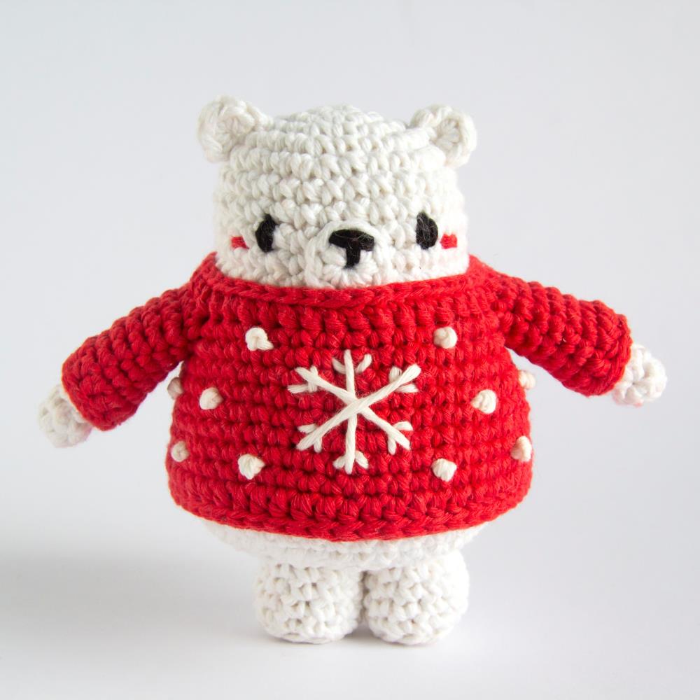 A crocheted polar bear in a red sweater embroidered with a snowflake design stands against a white background.