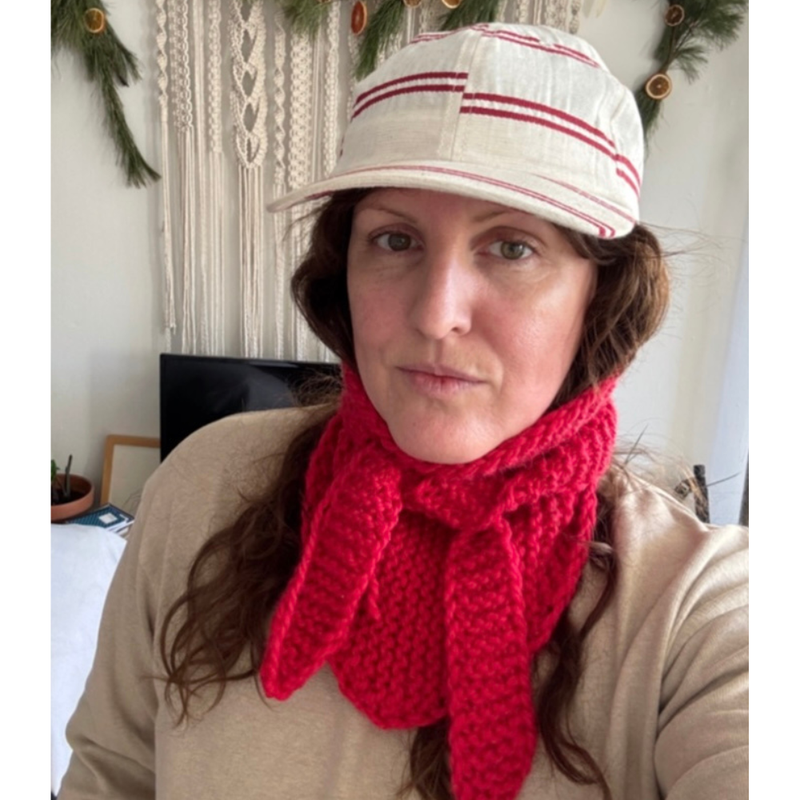 Person wearing a red knitted scarf and a striped cap indoors.