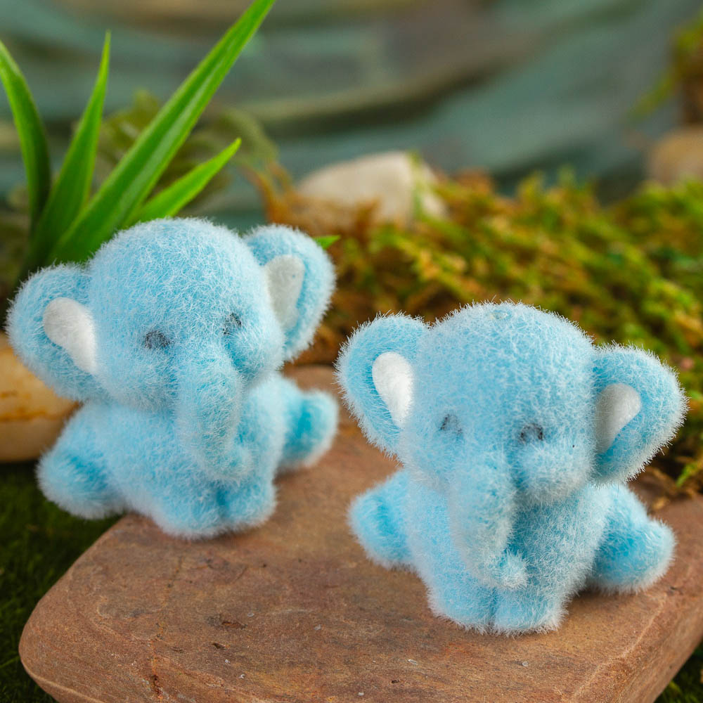 Two small blue fuzzy elephants on a rock with a natural background outdoors.