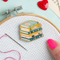 Wooden needle minder shaped like a stack of books on white aida fabric in an embroidery hoop