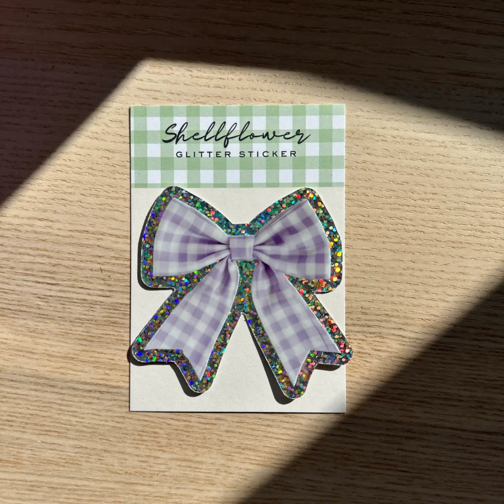 Glitter and gingham bow sticker on a checkered card with a wooden surface background