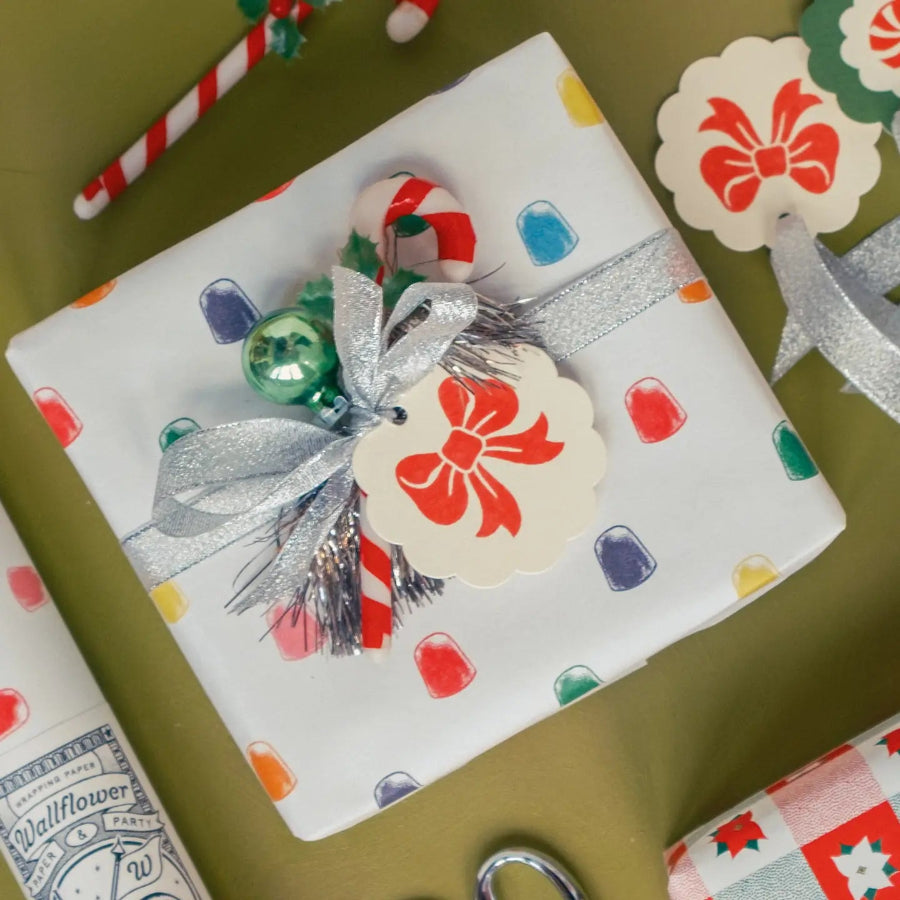 Gift wrapped in colorful paper with a silver bow and red tag on a green surface.