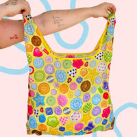 Colorful patterned bag held by a person against a pink background