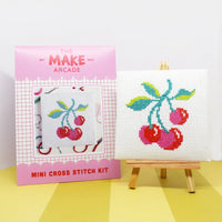 Cross stitch kit with cherry design on a white background, featuring 'The Make Arcade' packaging.
