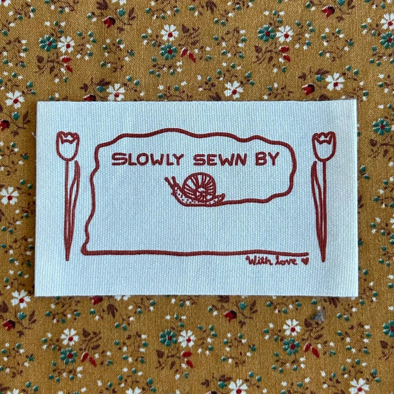Embroidered label with 'Slowly Sewn By' text on a floral fabric background