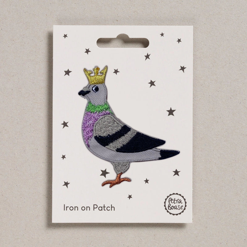 Embroidered patch of a pigeon with a crown on a white card with star patterns, branded 'Petra Boase'.
